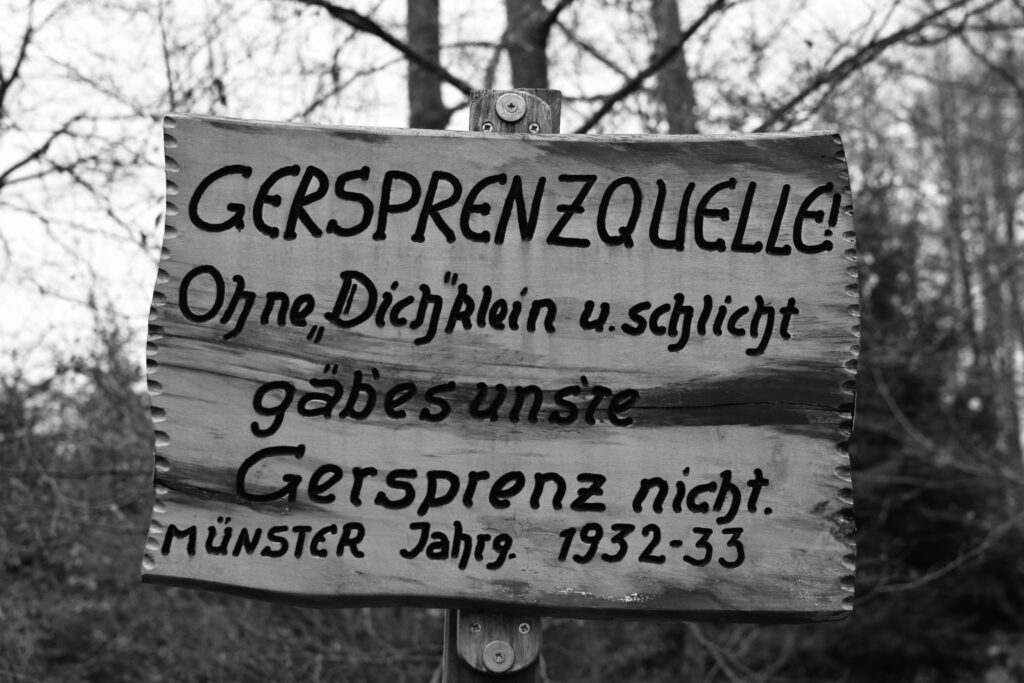 An der Gersprenzquelle hängt ein Holzschild mit der Aufschrift: „Gersprenzquelle! Ohne Dich, klein und schlicht, gäb' es uns're Gersprenz nicht. Münster, Jahrgang 1932-1933.“